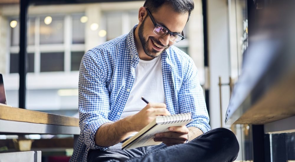 Мужчина сидит и пишет ручкой - SEO-оптимизированный описательный альт-текст для изображения.